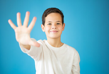 cool young boy smiling showing number five isolated on blue background