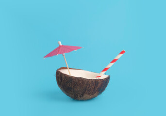 Tropical summer and vacation minimal concept. Coconut on a blue background with a cocktail straw. Vacation, travel, beach idea.