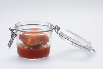 Clear glass jar with tomato gel and baked salmon on white background