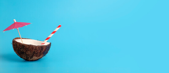 Tropical summer and vacation minimal concept. Coconut on a blue background with a cocktail straw. Vacation, travel, beach idea.