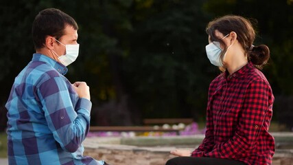 social distance. man and a girl in in protective face mask sitting on bench talking. pandemic coronavirus. two masked men observe greetings elbows avoid touching lifestyle. social distance covid 19