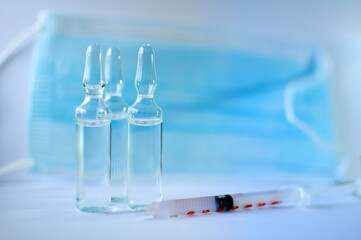 Vial vaccine, glass ampoules and a syringe with medical protective mask on white background, global vaccination concept