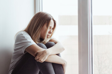 A young blonde beautiful despaired woman introvert in the white t-shirt and grey leggings is...