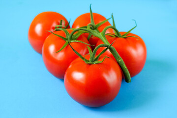 close-up of five ripe round red tomatoes in one bunch on a blue background side view . red raw vegetables