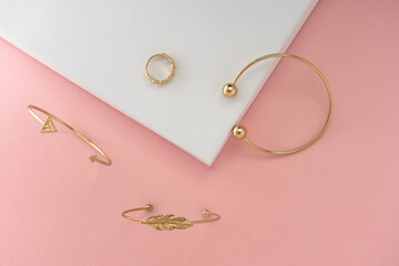 Modern design Golden bracelets and ring on pink and white background