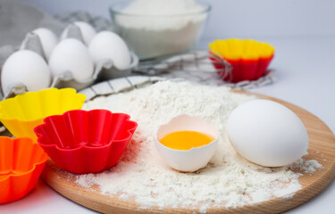 Flour, eggs and colourful silicone form on a table. Ingredients for baking muffins and cupcakes. Close-up.