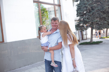 Fototapeta premium Three people, mother, father and daughter walking outdoor in the street of the city, people spending time with family together