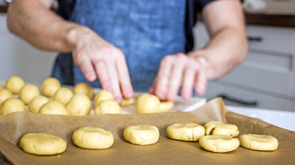 A faceless man in an apron in his kitchen at the kitchen table kneads bread dough  with his hands. Home authentic hobby, home baker. Baking bread with your own hands