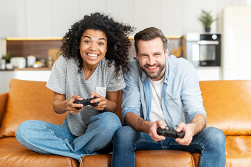 A multiracial couple enjoys time playing video game on the console, excited and tense young African woman and caucasian guy with a joysticks trying to win each other - Powered by Adobe