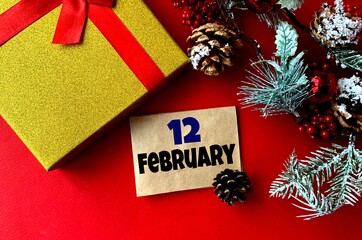 February 12 on craft paper. Near fir branches, cones, ribbon,gift box on a red background.Calendar for February.