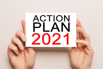 Female hands hold card paper with text ACTION PLAN 2021 on a yellow background. Business and finance concept