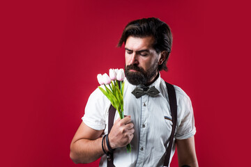 spring flower present. romantic man in suspenders and bow tie. confident and elegant man hold tulip flowers. gift for love date. old fashioned bearded hipster with bouquet