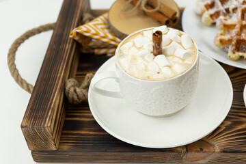 Early breakfast coffee with marshmallows and a stick of cinnamon and Belgian waffles lie on a wooden tray