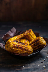 Grilled corn on the cob on black cooking pan with salt in the air. Wooden rustic table,  dark background. Grilled vegetables, vegetarian food, bbq. Copy space, dark mood photography.