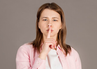 Portrait of brown-haired gorgeous attractive nice cute funny smililng young lady showing shhh taboo sign with finger to lips over grey background, isolated