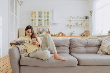 Attractive woman with a bionic arm sits at home on the couch in comfortable home clothes with a...
