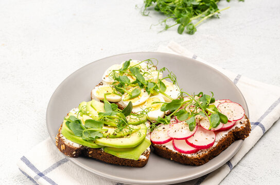 Different sandwiches with radishes, avacado, egg and microgreens on a gray plate on a light background.