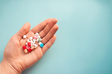 Colorful pills and capsules in a person's hand on a blue background with copy space
