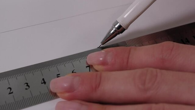 A seamstress with a ruler draws a pattern on paper with a pencil, the process of making clothes in a sewing workshop.