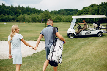 Fototapeta premium Couple in a golf course. Blonde in a sport clothes. Pair playing golf