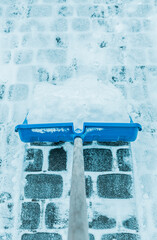 Snowy winter - blue shovel removing snow from the paver path (sidewalk)