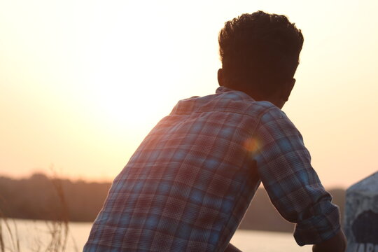 Man Looking Away While Sitting Against Sky During Sunset