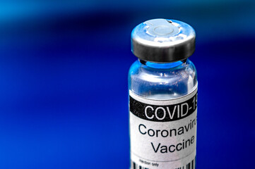 Medical vial for injection on blue background. Glass ampoule with the inscription COVID-19 VACCINE