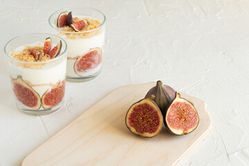 Fresh figs are whole, lying in halves on a wooden board. In the background is a dessert of fruit in...