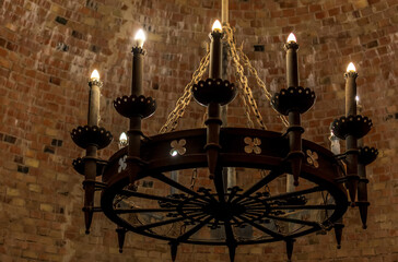 Old vintage candelabrum with twelve candles, hanging on rusty chain against red brick wall inside the tower of Turaida Medieval Castle, Latvia.