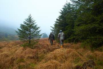 Two hunters in the forest during the day with moss and grass.