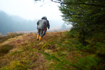 Two hunters in the forest during the day with moss and grass.