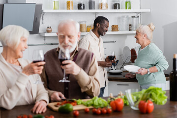 African american man and happy senior woman looking at each other near retired friends on blurred foreground