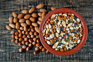 Many types of nuts close up. Texture of different nuts on a wooden board. Clay bowl on a brown table.