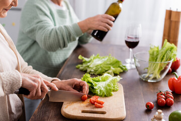 cropped view of retired woman cutting cherry tomato on cutting board