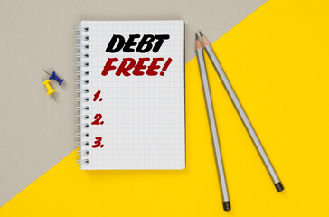 On a yellow-gray background are pencils, buttons and a notebook in which it is written - DEBT FREE