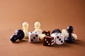 The dice are brown and white and chess pieces of white and black pawns close up on a brown...