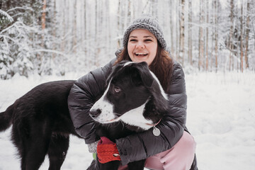 cheerful Young girl embracing her big black dog in winter snowy forest. Domestic pets with owners. Best friends.