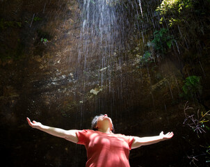 Fototapeta na wymiar Mulher de braços abertos embaixo de uma cascata de água em uma gruta natural.