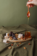 Fototapeta na wymiar Set for Tea drinking. Hand holding spoon with dripping honey. Various sweets, nuts and honey for tea on a wooden cutting board. Healthy sweets, delicious dessert, natural sweets.