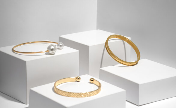 Three modern golden bracelets on white geometric boxes