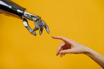 Foto op Plexiglas Robotic bionic hand and a woman's hand pulling fingers together on a yellow background close-up, the concept of human interaction and modern technology © wifesun