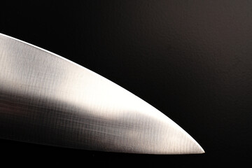 The blade of a large knife on a black background. Dimmed lights.