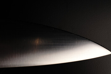 The blade of a large knife on a black background. Dimmed lights.