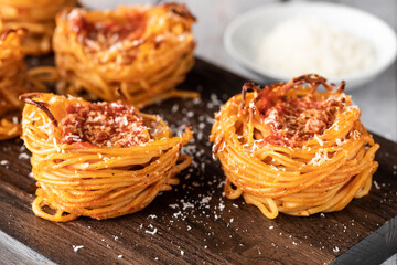 Close up of spaghetti nests sprinkled with parmesan cheese on a wooden board.