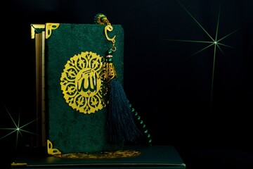 Green cover Holy Quran with arabic word Allah meaning The One and Only God and tasbih or rosary...