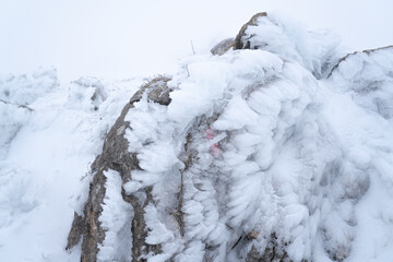 Image of trail marker in the mountains on the hiking trail. White and red way marker sign painted on a  frozen rock. Cold weather concept.