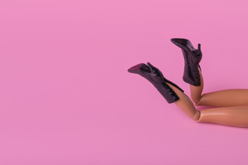 Creative composition with doll legs in boots with high heels on pastel pink background