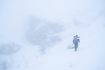 Fototapeta na wymiar IMAGE OF A PERSON HIKING IN EXTREME CONDITIONS. ALPINIST TREKKING IN HARSH WINTER CONDITIONS. COLD AND BAD WEATHER CONCEPT