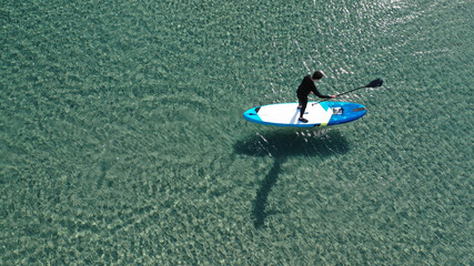 Fototapeta premium Aerial drone photo of fit man on SUP or Stand Up Paddle board in tropical exotic emerald calm sea bay