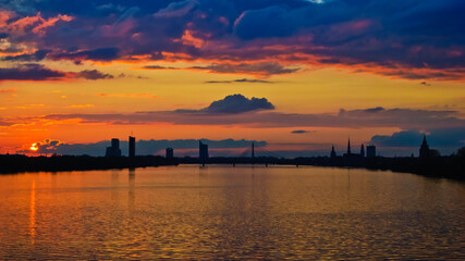 Naklejka premium sunset. in the photo, the clouds are illuminated by the evening sun,in the foreground is a river, in the background is a city